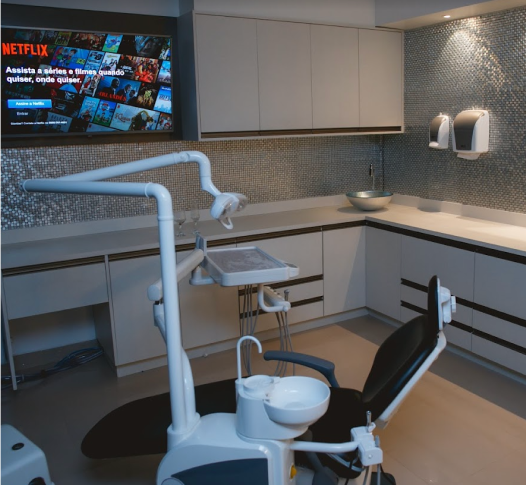 Um consutório com tecnologia de ponta, mostrando uma TV e uma cadeira de dentista branca