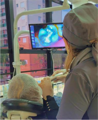 Doutora Ivani usando uma camera intra oral no paciente mostrando a ele em tempo real como estão seus dentes e falando o que se deve ou não fazer.