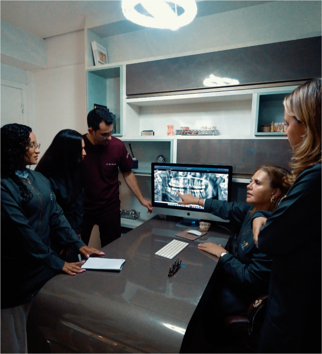 Cinco doutores reunidos, analisando minuciosamente um raio X panorâmico e discutindo estratégias de tratamento para o paciente.