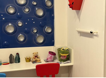 Doutora Adrielly chamando a paciete criança para entrar no consultório, enquano outros pacientes e seus pais aguardam na sala de espera infantil