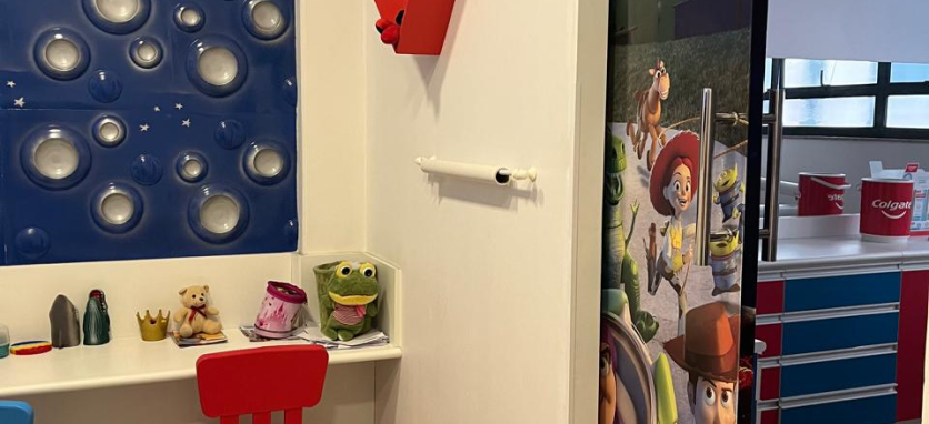 Doutora Adrielly chamando a paciete criança para entrar no consultório, enquano outros pacientes e seus pais aguardam na sala de espera infantil