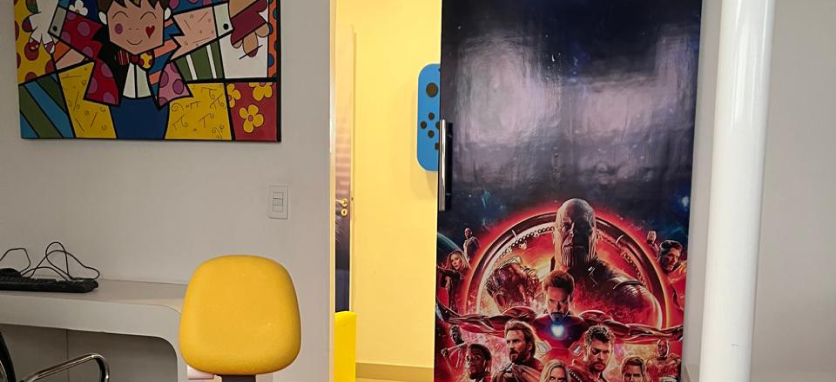 Doutora Adrielly chamando a paciete criança para entrar no consultório, enquano outros pacientes e seus pais aguardam na sala de espera infantil